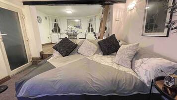 A bedroom with a large bed, a bedside table, a mirror, and a view into the dining area.