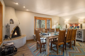 Un coin repas avec une cheminée, des chaises en bois, une table et un tapis à motifs.