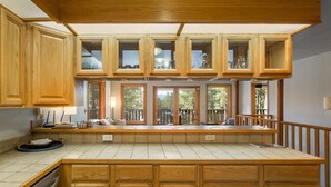 A kitchen with wooden cabinetry, a built-in island, and large windows offering a view of the outdoors. - Cabin Walkable to Lake with Hot Tub, Deck & Views, Pool Table, Near Golf & Bike (Angel Fire)
