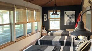 Quarto com duas camas, uma janela grande, um ventilador de teto e uma luminária fixada na parede.