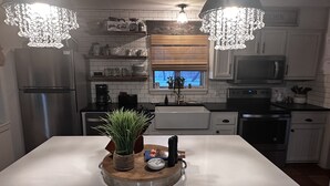 Cozinha moderna com armários brancos, eletrodomésticos de aço inoxidável e uma ilha central com planta e objetos decorativos.