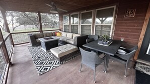 Uma área de varanda coberta com sofá, puf e mesa, lareira e ventilador de teto.