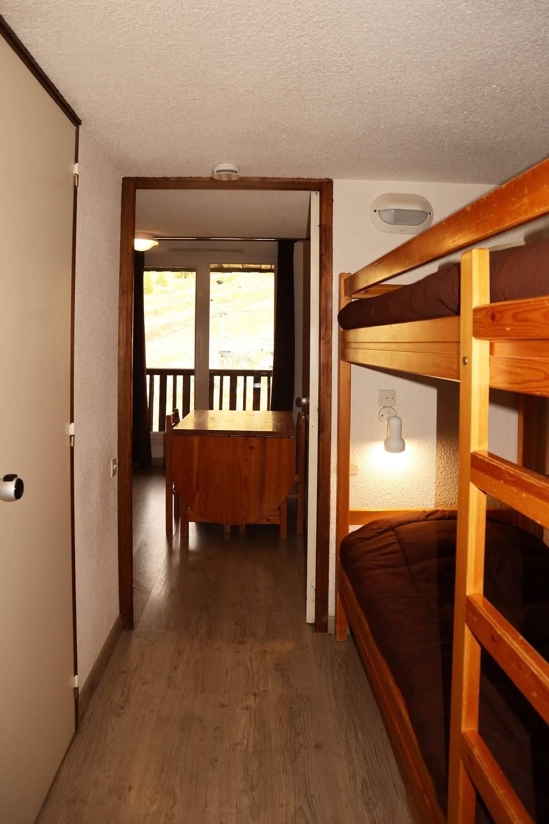 A wooden bunk bed with a headboard, a wooden dining table with chairs, and a view of a balcony with a railing.