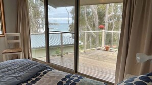 A bedroom with a large sliding glass door leading to a balcony with a view of the sea and trees. - Seascapes at Rosedale (ROSEDALE)