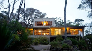 A modern two-story house with large windows, surrounded by dense vegetation. - Seascapes at Rosedale (ROSEDALE)