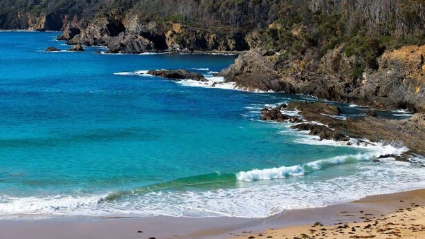 A coastal landscape with rocky cliffs, clear blue waters, and a sandy beach. - Seascapes at Rosedale (ROSEDALE)