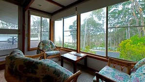 A room with large windows, wicker furniture, and a view of trees. - Seascapes at Rosedale (ROSEDALE)