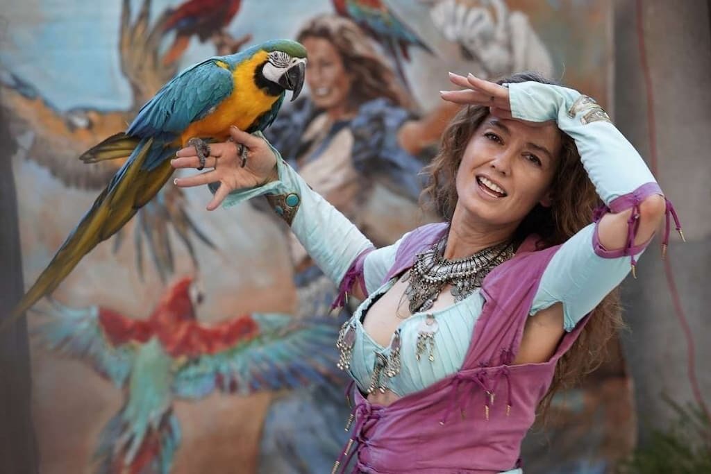 A person holding a parrot with a mural of colorful birds in the background.