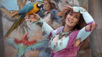 A person holding a parrot with a mural of colorful birds in the background.