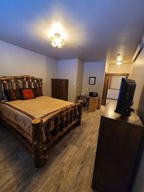 A bedroom with a rustic bed frame, a wooden dresser, a television on a stand, and a door leading to another room. - Star Valley Lodge (Bedford)
