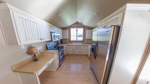 Una cocina con armarios blancos, encimera de madera, refrigerador de acero inoxidable y ventana con vistas al exterior.