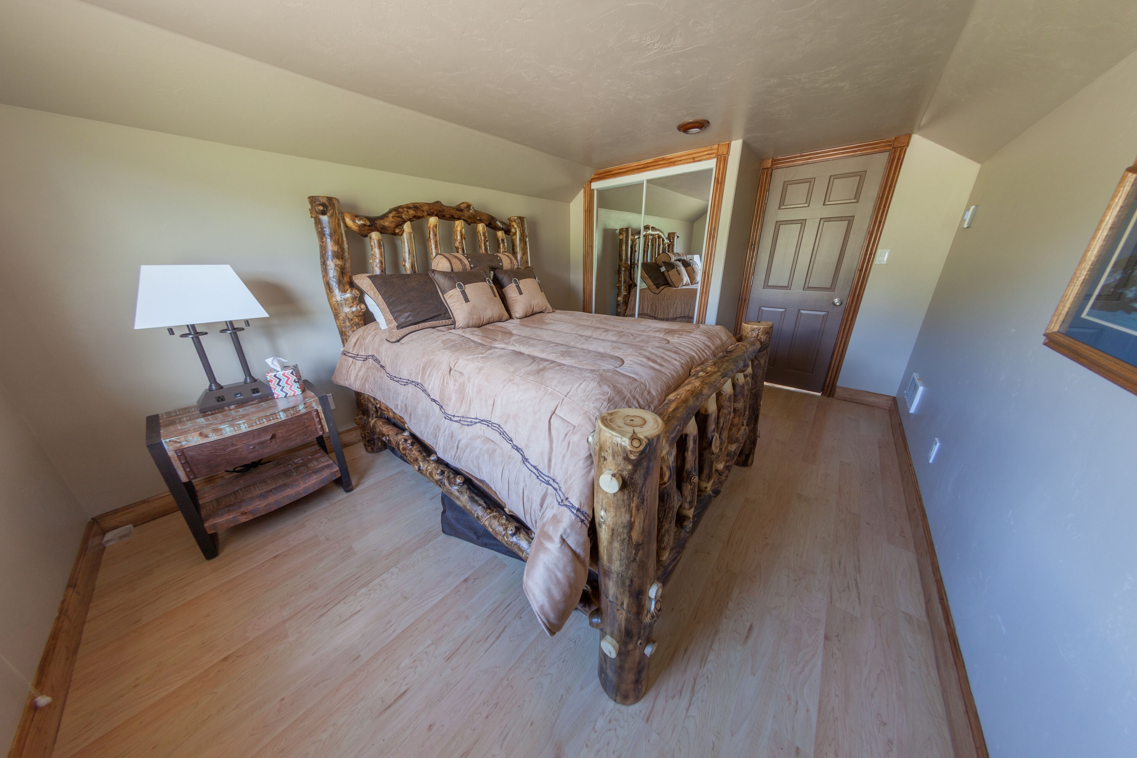 A bedroom with a large bed, a nightstand, a mirror, and a door.