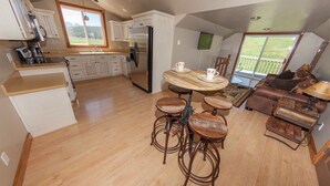 Una cocina moderna con armarios blancos, un refrigerador de acero inoxidable y un comedor con una mesa redonda y taburetes.