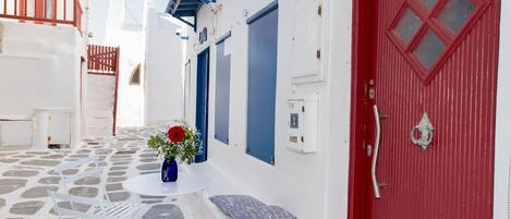 A narrow street with white buildings, a red door, and a small table with a vase of flowers.