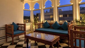 A room with a checkered floor, a wooden sofa with teal cushions, a wooden coffee table, and a window with decorative cutouts. - Amar Mahal Luxury Boutique Hotel Near Fateh Sagar Lake, Udaipur (Udaipur)
