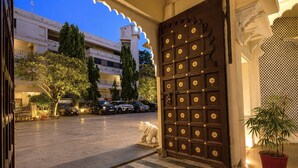 A hotel entrance with a large ornate door, a stone-paved courtyard, and a building in the background. - Amar Mahal Luxury Boutique Hotel Near Fateh Sagar Lake, Udaipur (Udaipur)