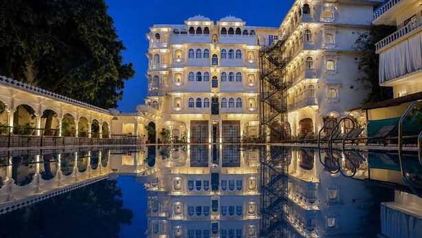 A multi-story building with a reflective pool in front, featuring traditional architecture with arched windows and balconies. - Amar Mahal Luxury Boutique Hotel Near Fateh Sagar Lake, Udaipur (Udaipur)