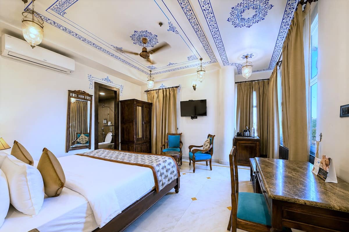 A hotel room with a bed, a desk, a chair, a television, and a ceiling fan.