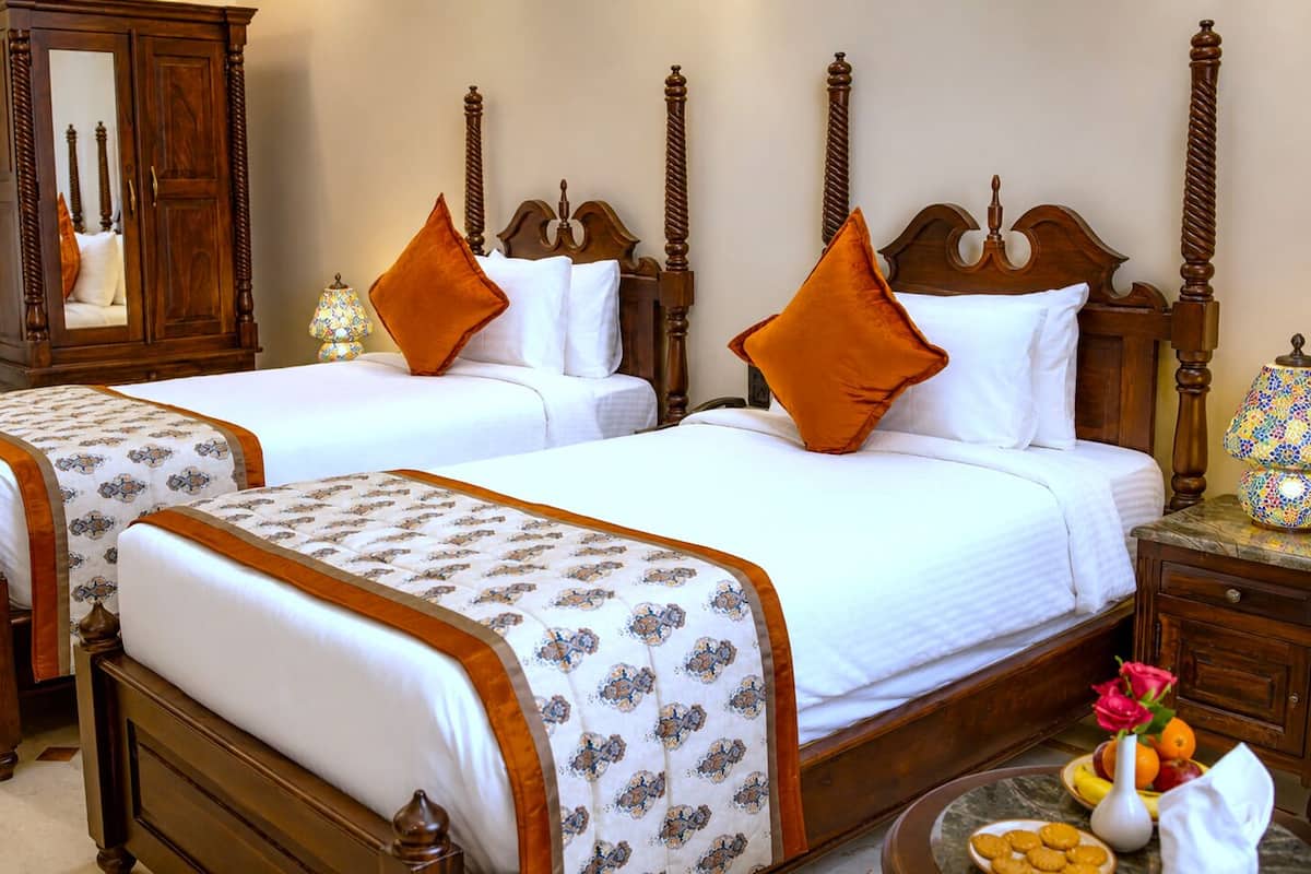 A hotel room with two double beds, wooden headboards, a nightstand with a lamp, and a mirror.
