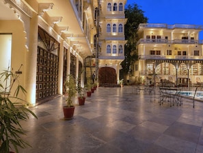 A hotel courtyard with tiled flooring, potted plants, outdoor seating, and a pool. - The Amar Mahal (Udaipur)