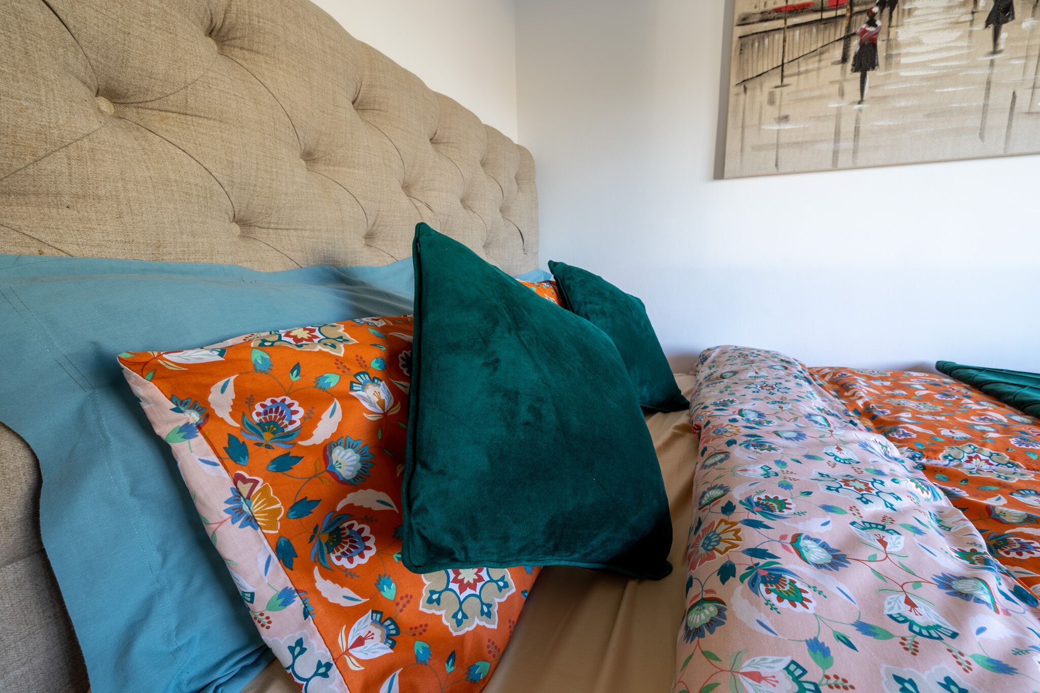 A bed with a tufted headboard, floral-patterned bedding, and a painting on the wall.