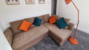 Una sala de estar con un sofá seccional marrón, cojines naranja y aguamarina, y una lámpara de pie roja.