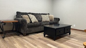 A room with a dark grey sofa, patterned cushions, a small wooden side table, and a black cabinet. - Unique Space in Historic Building (Osborne)