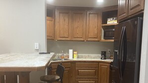 A kitchen with wooden cabinets, a black refrigerator, a marble countertop, and a bar stool. - Unique Space in Historic Building (Osborne)