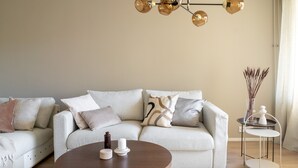 Ett vardagsrum med en beige soffa, ett runt soffbord i trä och en modern kristallkrona.