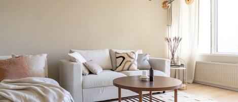 A modern living room with a light grey sofa, a round wooden coffee table, and a white rug.