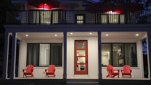 Una casa moderna de dos pisos con un balcón, sillas rojas y una puerta roja.