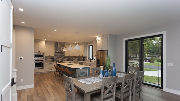 Una cocina moderna con armarios blancos, una isla grande y un comedor con sillas y una mesa de madera.