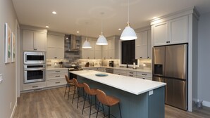 Una cocina moderna con una isla central, taburetes de bar, electrodomésticos de acero inoxidable e iluminación colgante.