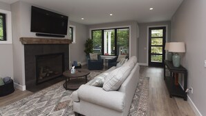 Una sala de estar moderna con chimenea, un sofá grande, un televisor y vistas al exterior.