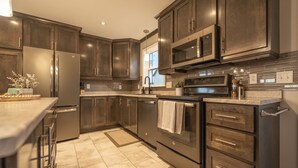 A modern kitchen with dark wood cabinets, stainless steel appliances, and a tiled floor.