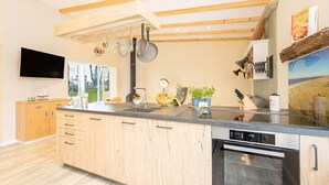 Eine moderne Küche mit Holzschränken, einem eingebauten Ofen und einer großen Kochinsel mit Spüle und Arbeitsplatte.