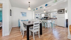 A modern kitchen with white cabinetry, a central island, and a dining area with a wooden table and white chairs. - LakeView Getaway: Lake views & hot tub! (Lexington)