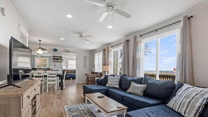 A modern living room with a dark blue sofa, a wooden coffee table, and a view of the ocean through large windows. - LakeView Getaway: Lake views & hot tub! (Lexington)