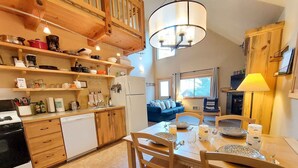 A kitchen with wooden cabinets, a dining table with chairs, a refrigerator, and a chandelier.