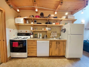 A compact kitchen with a gas stove, white dishwasher, and a white refrigerator.