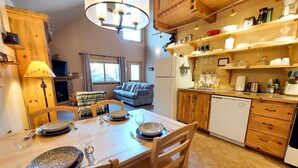 A cozy kitchen with wooden cabinets, a dining table set for four, and a living area with a sofa and a TV. - Alpine View Cabin - duplex unit B w/ queen bedroom (Winthrop)