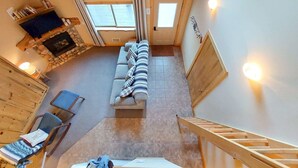 A high-ceilinged room with a fireplace, a sofa, a chair, and a wooden staircase. - Alpine View Cabin - duplex unit B w/ queen bedroom (Winthrop)