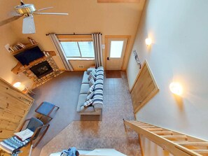 Ein Zimmer mit hohen Decken, ausgestattet mit Kamin, einer Couch, einem Sessel und einer Holztreppe.
