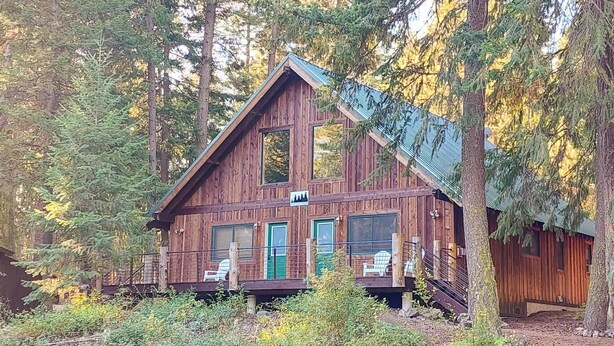 A cabin with a porch, a chimney, and a window with a view of the forest. - Alpine View Cabin - duplex unit B w/ queen bedroom (Winthrop)