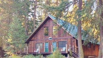 Una cabaña con porche, chimenea y ventana con vistas al bosque.