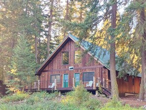 A cabin with a porch, a chimney, and a window with a view of the forest. - Alpine View Cabin - duplex unit B w/ queen bedroom (Winthrop)