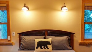 A bed with a headboard, two wall-mounted lights, a window with a view of trees, and a power outlet. - Alpine View Cabin - duplex unit B w/ queen bedroom (Winthrop)