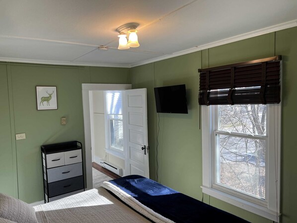 A room with a bed, a dresser, a television, a window with blinds, and a ceiling fan.
