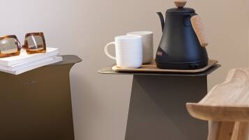 A coffee maker on a tray with two white mugs and a pair of glasses on a table.