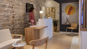 A reception area with a stone wall, wooden reception desk, and a modern chair. - Le Daum (Paris)